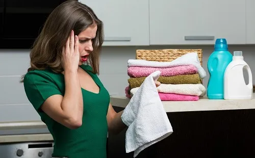 Девушка в зеленом платье смотрит на пятна на полотенце после стирки в стиральной машине