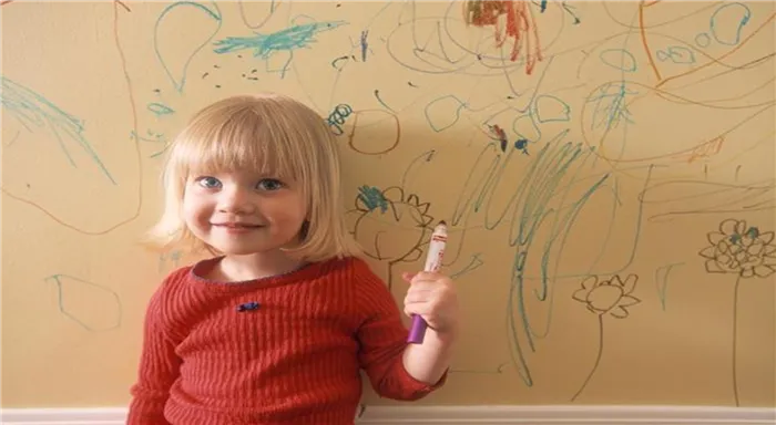 Маленькая девочка рисует на стене фломастером.