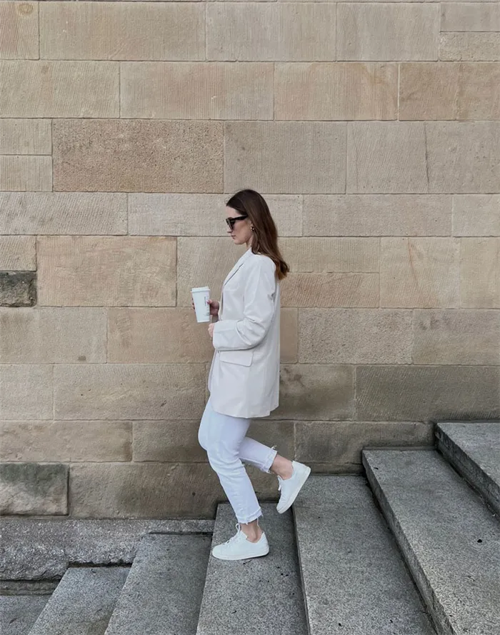 Девушка в белых джинсах, длинной куртке, белых кроссовках
