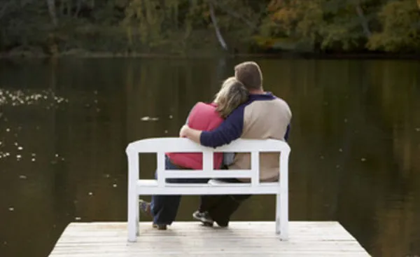 Влюбленная пара сидит на скамейке перед рекой, на мосту