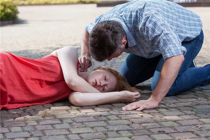 Молодая девушка упала в обморок, мужчина уложил ее на бок, оказывает помощь