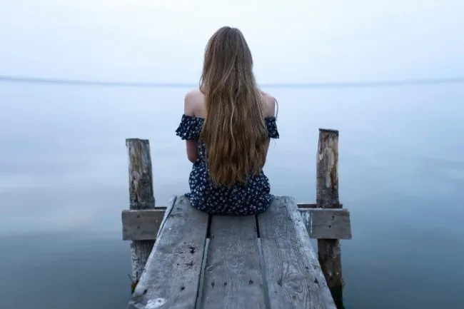Девушка сидит на мостках и смотрит на море