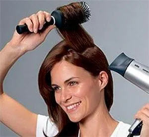 девушка делает прикорневой объём волос при помощи фена и брашинга