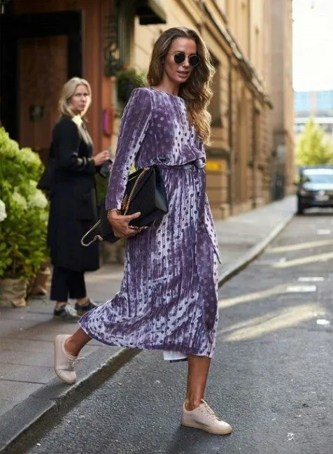 Яркое плисовое фиолетовое платье в горошек в сочетании с нежными нюдовыми кроссовками. Образ дополнен черной сумкой и очками.