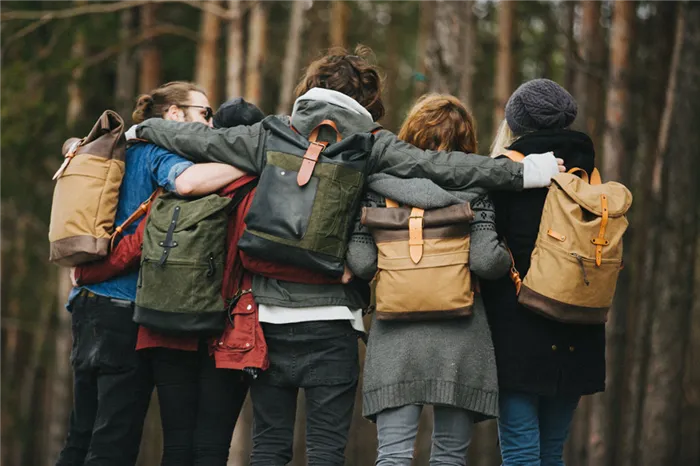 Молодые люди стоят в лесу в обнимку спиной к объективу с рюкзаками на плечах