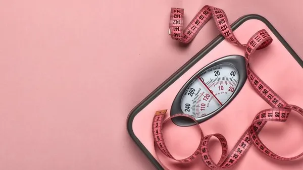 Весы и сантиметр на розовом фоне.