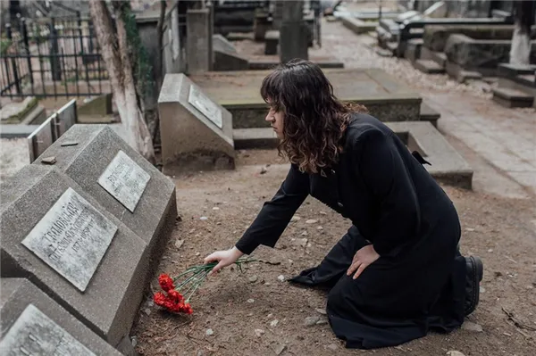 Женщина в черном кладет цветы на могилу
